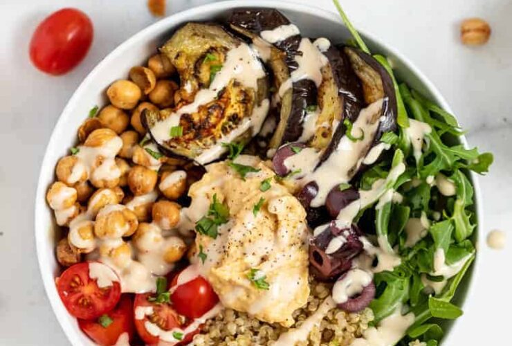 Colorful quinoa bowls topped with roasted red pepper sauce and fresh Mediterranean ingredients.