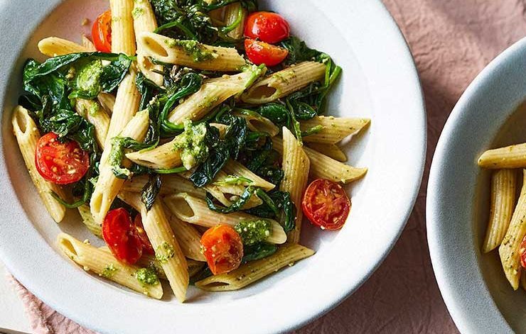 Bowl of penne pasta coated in vibrant green pesto sauce.