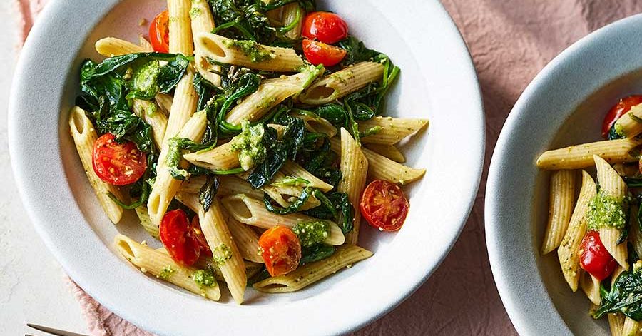 Bowl of penne pasta coated in vibrant green pesto sauce.