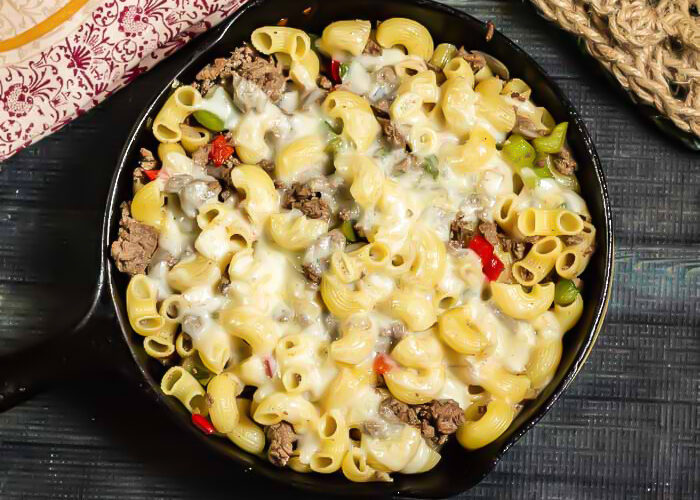 Skillet meal with pasta, thinly sliced steak, onions, peppers, and melted cheese.