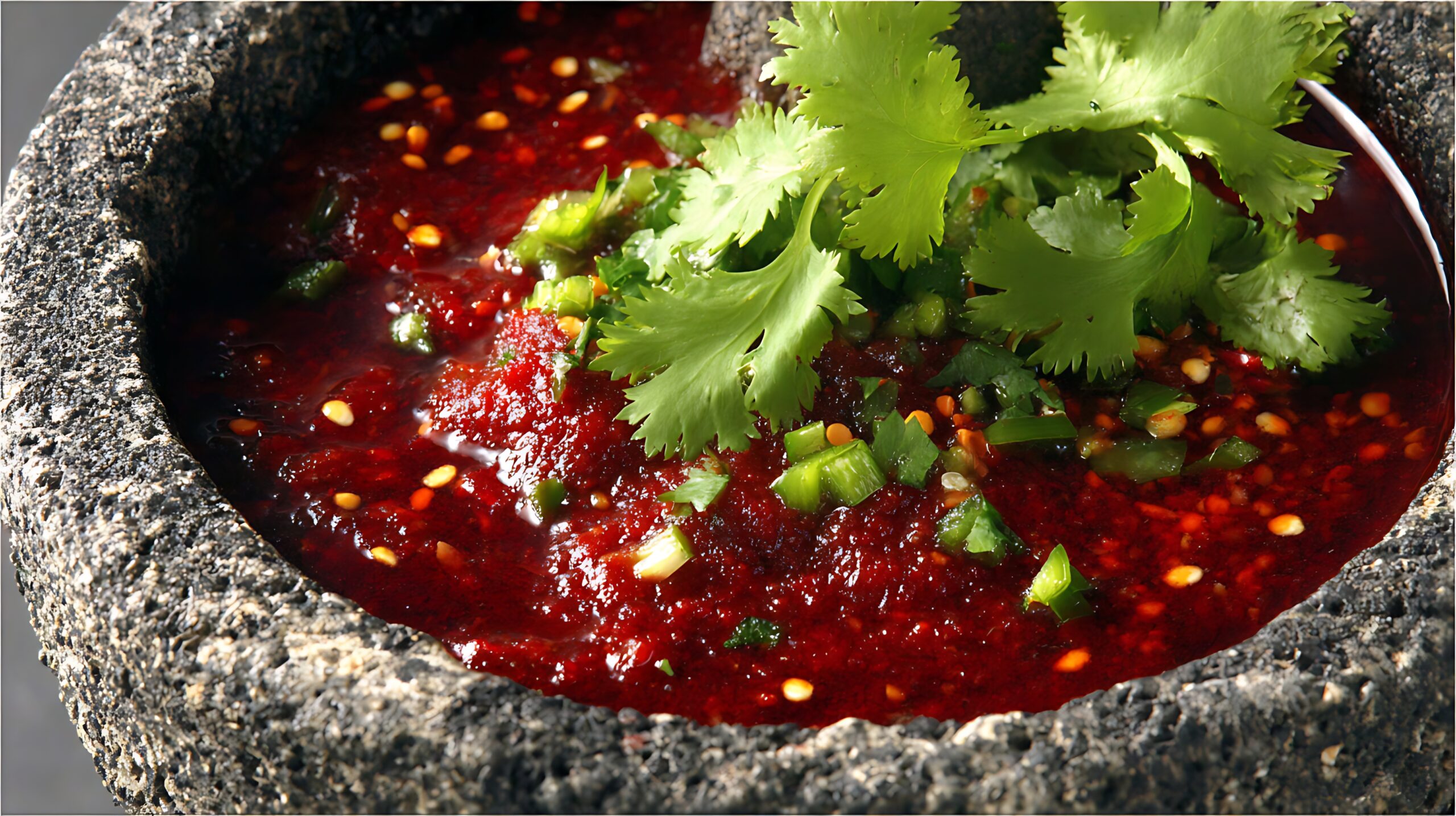 Soaked habaneros and arbol chilies in a clear bowl next to oil-roasted Roma tomatoes with their skins beginning to peel