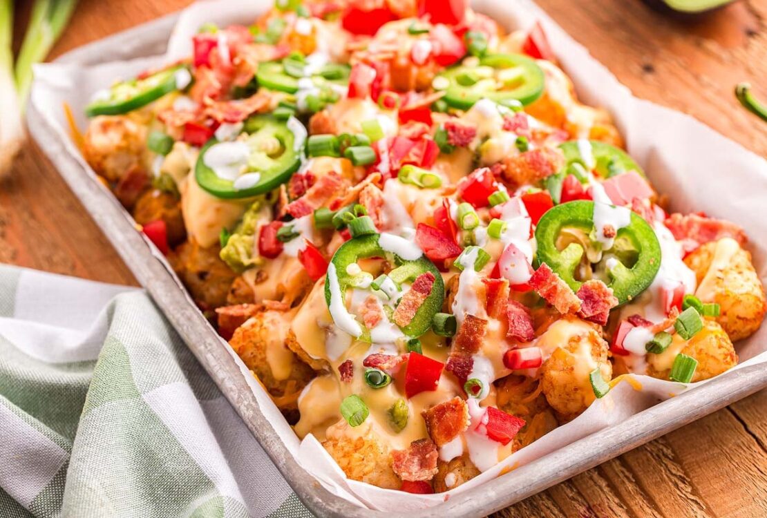loaded tater tot nachos on large platter with melted cheese, ground beef, jalapeños, and fresh toppings