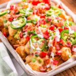 loaded tater tot nachos on large platter with melted cheese, ground beef, jalapeños, and fresh toppings