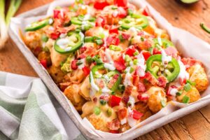 loaded tater tot nachos on large platter with melted cheese, ground beef, jalapeños, and fresh toppings