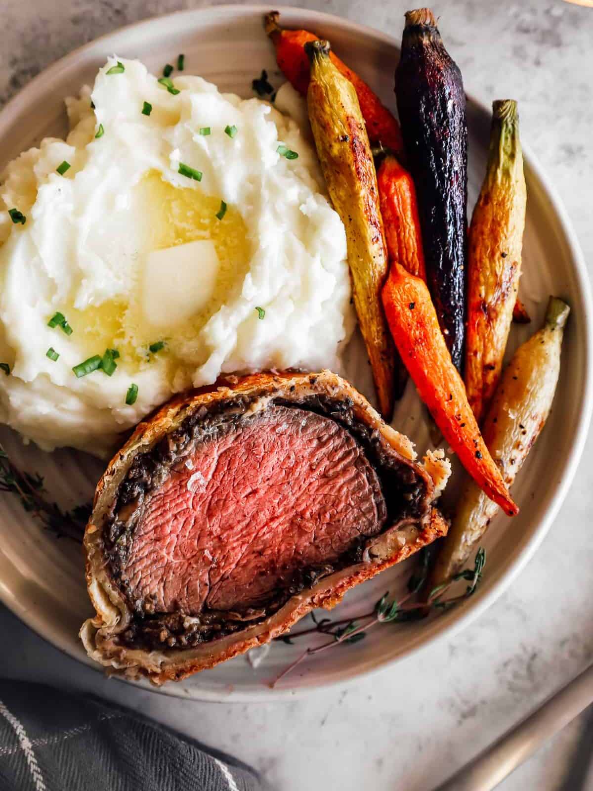 beef wellington slice on plate with roasted vegetables and red wine reduction sauce