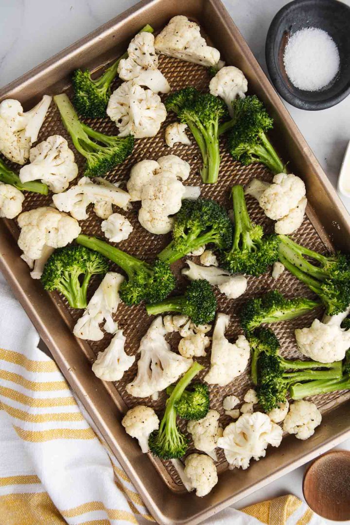 raw broccoli and cauliflower florets tossed with olive oil on sheet pan before roasting