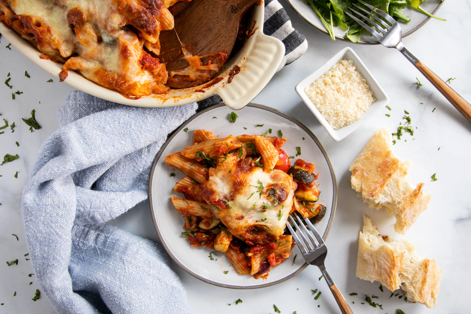 close-up of a serving of pasta bake on white plate showing melted cheese and roasted vegetables