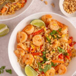 Authentic pad thai noodles with shrimp bean sprouts lime wedges and crushed peanuts on white plate