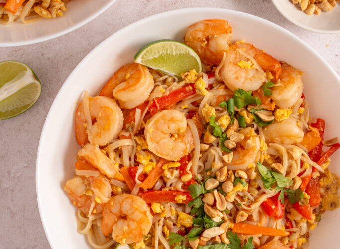 Authentic pad thai noodles with shrimp bean sprouts lime wedges and crushed peanuts on white plate