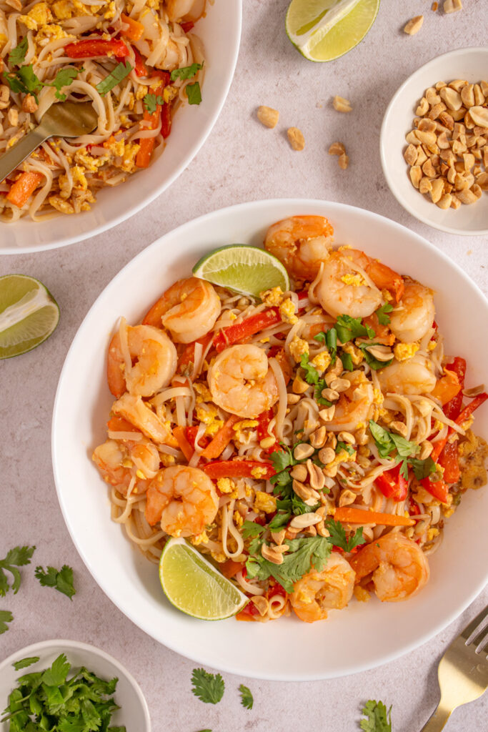 Authentic pad thai noodles with shrimp bean sprouts lime wedges and crushed peanuts on white plate