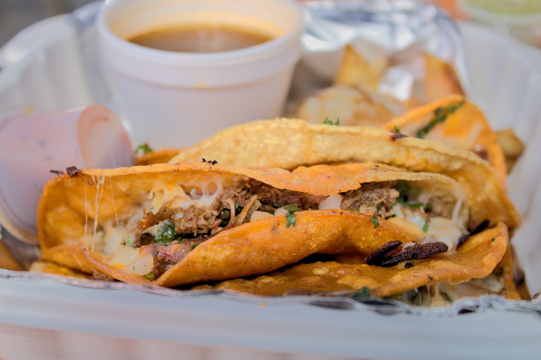 Close-up shot of a birria taco being dipped into a small clay bowl of rich, red consomm? with melted cheese stretching between the taco and bowl