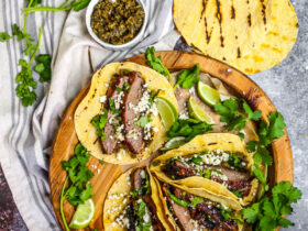 Beautifully plated carne asada tacos with charred beef, fresh cilantro, diced onions, and lime wedges on rustic wooden serving board