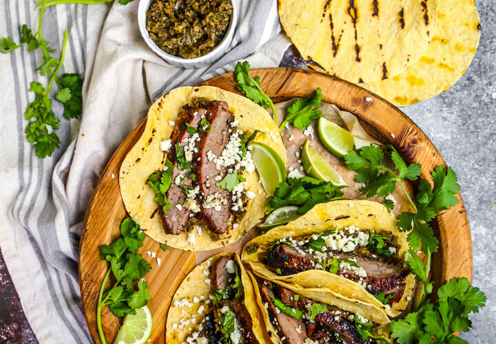 Beautifully plated carne asada tacos with charred beef, fresh cilantro, diced onions, and lime wedges on rustic wooden serving board