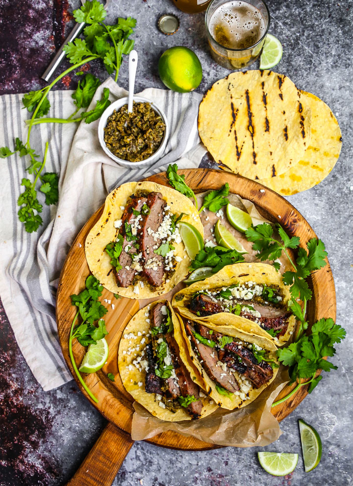 Beautifully plated carne asada tacos with charred beef, fresh cilantro, diced onions, and lime wedges on rustic wooden serving board