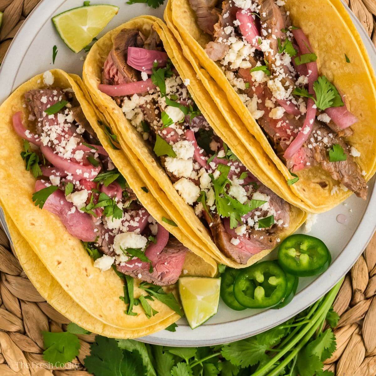 Close-up shot of a perfectly assembled carne asada taco showing charred beef strips, fresh cilantro, and diced onions with lime wedge on the side