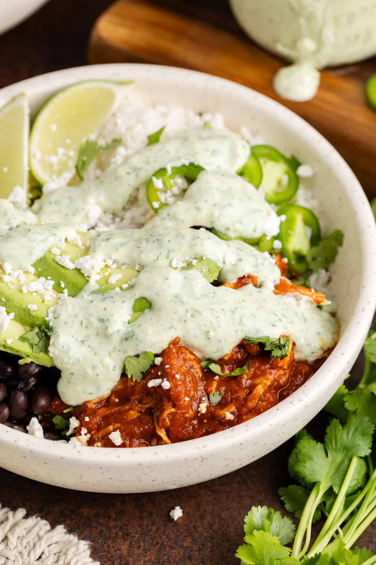 Close-up of chicken tinga in a blue ceramic bowl garnished with fresh lime wedges, cilantro, and a dollop of Greek yogurt