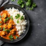 Creamy butter chicken served in a black bowl with basmati rice and fresh cilantro garnish