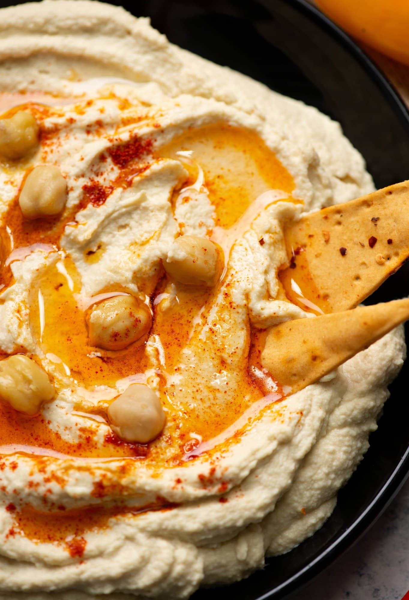 Creamy homemade hummus in a white bowl with olive oil drizzled on top, garnished with chickpeas and paprika, surrounded by fresh vegetables and pita bread
