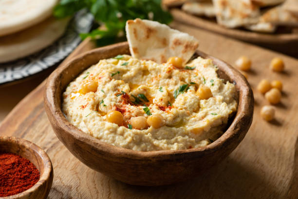 Close-up shot of creamy hummus being scooped with a pita chip, showing the smooth, velvety texture with olive oil pooling slightly