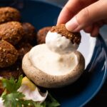 Golden crispy falafel balls arranged on a white plate with tahini drizzle, fresh parsley, and colorful vegetables