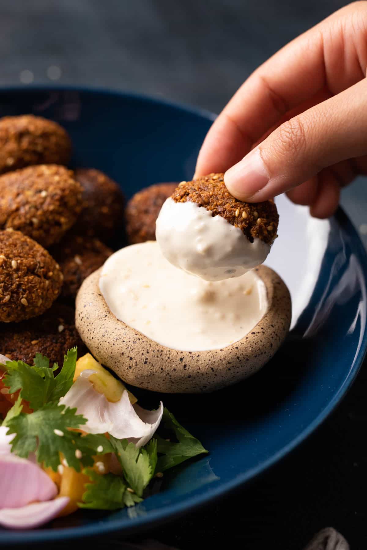 Golden crispy falafel balls arranged on a white plate with tahini drizzle, fresh parsley, and colorful vegetables