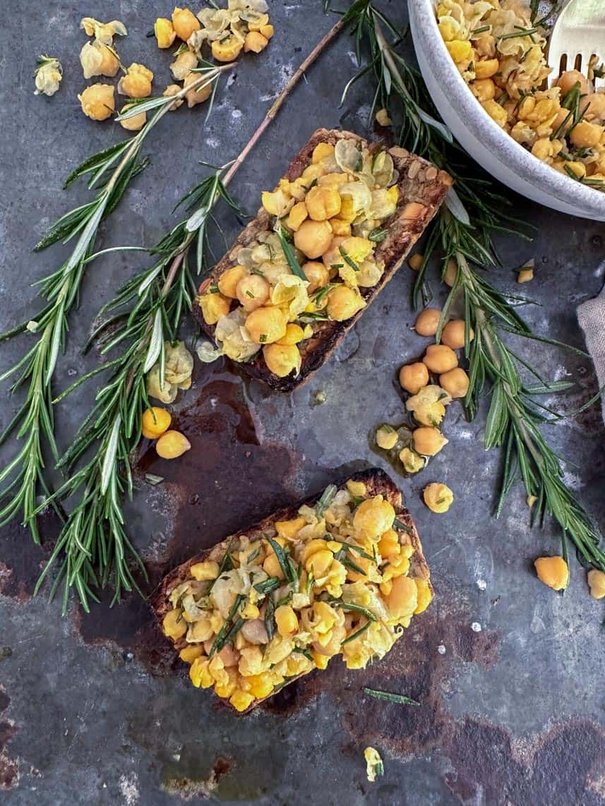 Chickpeas soaking in a glass bowl next to fresh herbs and spices laid out on a cutting board