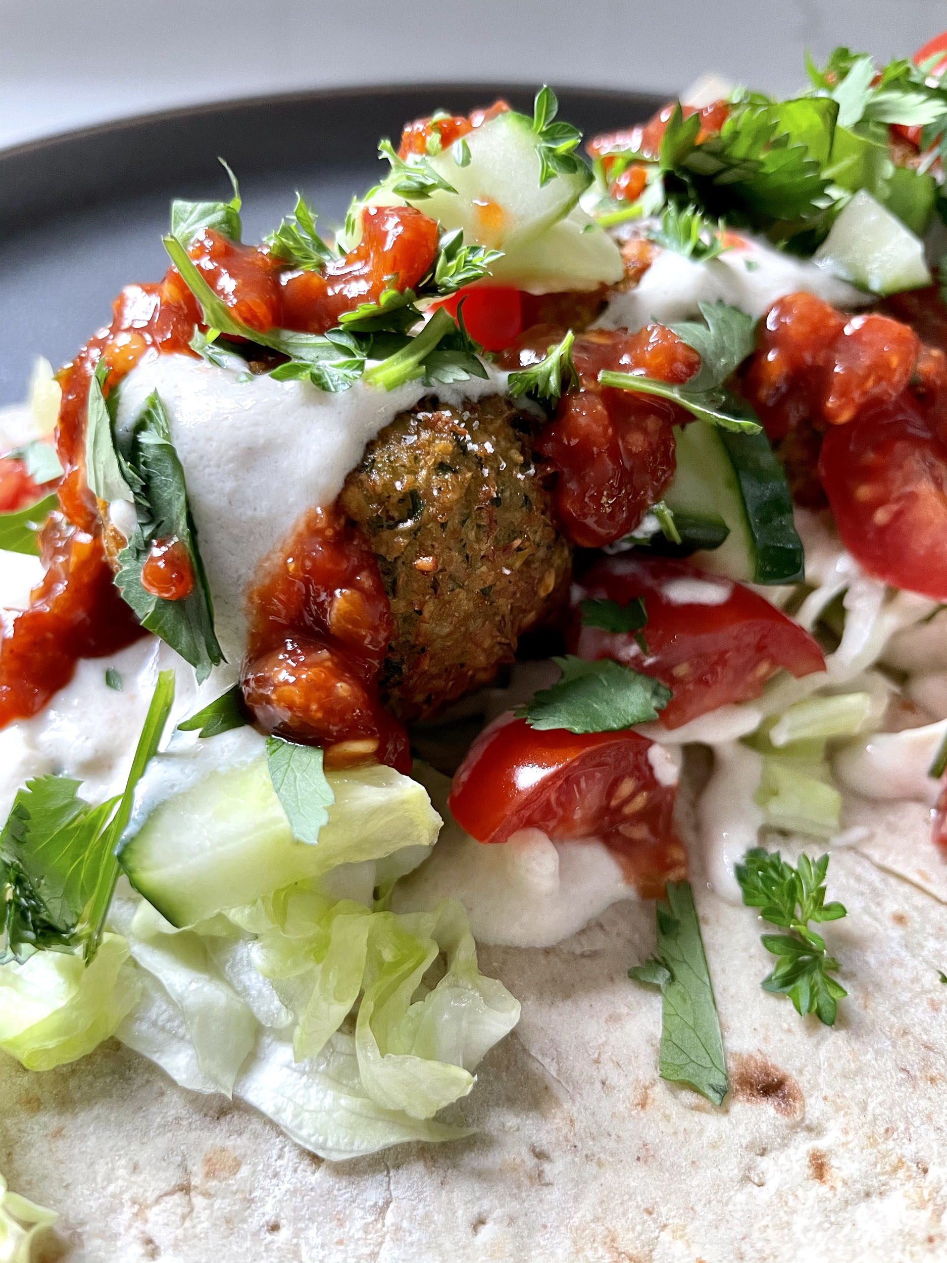 Close-up shot of a halved falafel showing the fluffy green interior with herbs visible, served with tahini sauce drizzling down