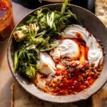 Eggs in harissa sauce with whipped goat cheese served in cast iron skillet with fresh herbs and crusty bread