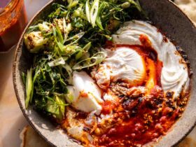 Eggs in harissa sauce with whipped goat cheese served in cast iron skillet with fresh herbs and crusty bread