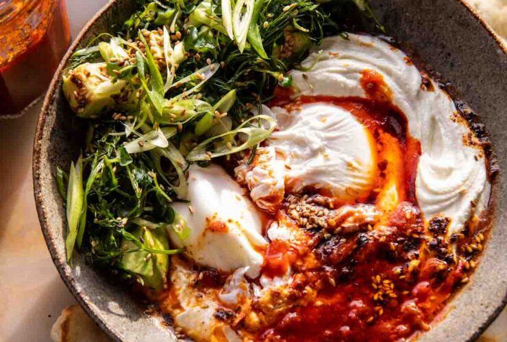 Eggs in harissa sauce with whipped goat cheese served in cast iron skillet with fresh herbs and crusty bread