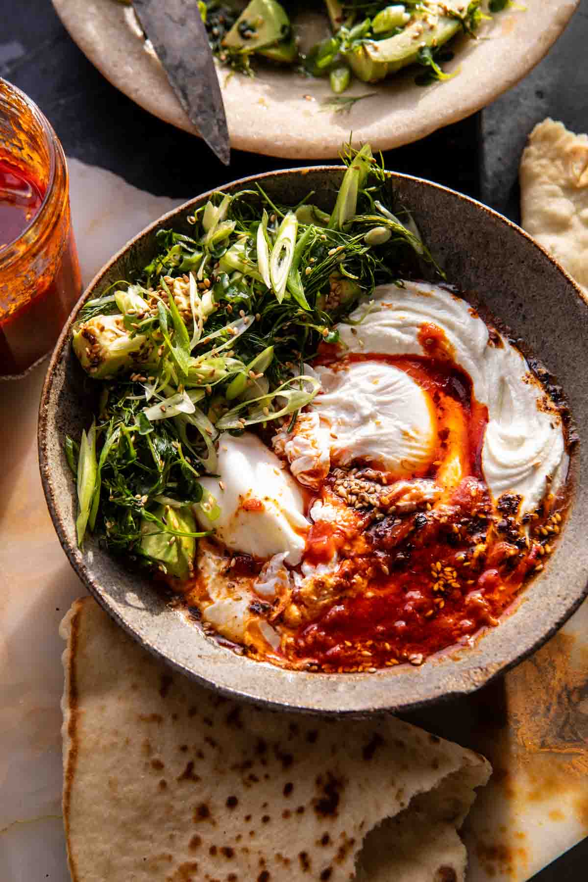 Eggs in harissa sauce with whipped goat cheese served in cast iron skillet with fresh herbs and crusty bread