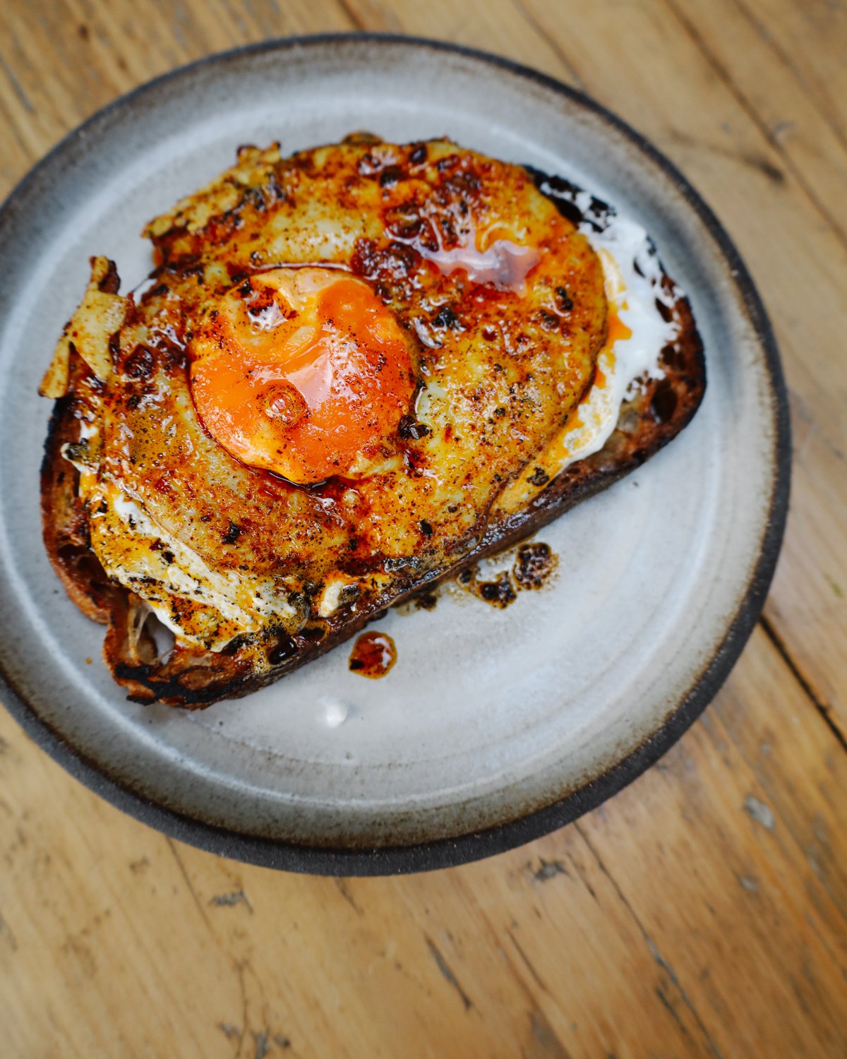 Close up shot of runny egg yolk mixing with harissa sauce and goat cheese on rustic bread