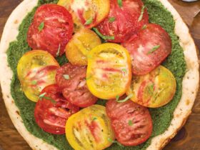 Overhead shot of heirloom tomato and pesto pizza with colorful tomato varieties arranged on golden crust with fresh basil garnish