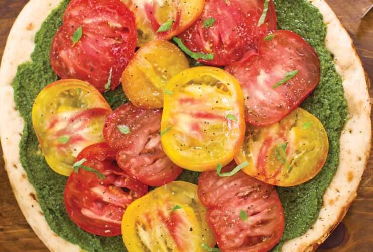 Overhead shot of heirloom tomato and pesto pizza with colorful tomato varieties arranged on golden crust with fresh basil garnish
