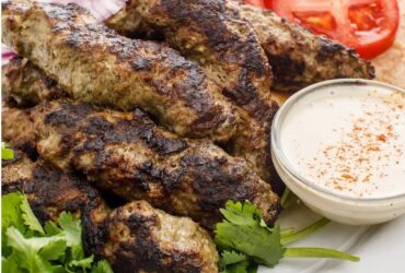 Lebanese kafta kebabs beautifully arranged on a white platter with fresh herbs, grilled vegetables, and warm pita bread alongside tahini sauce