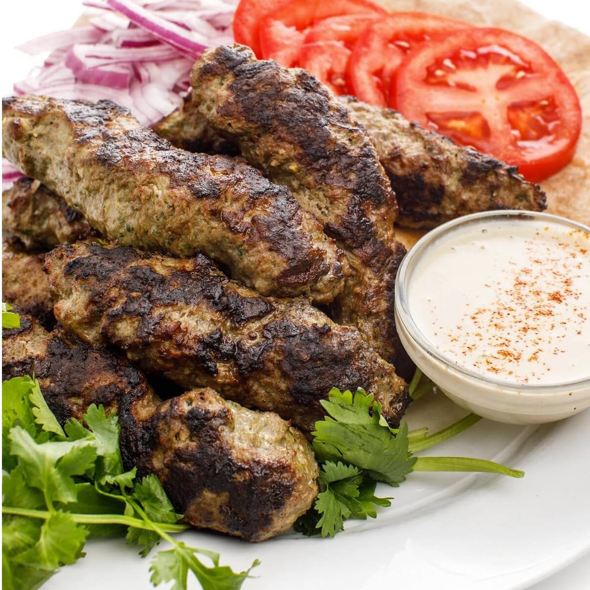 Lebanese Kafta Kebabs: Healthy Grilled Perfection with Aromatic Spices 26 Lebanese kafta kebabs beautifully arranged on a white platter with fresh herbs, grilled vegetables, and warm pita bread alongside tahini sauce