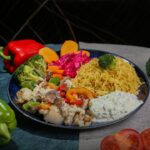 Mediterranean chicken bowl with golden herb-crusted chicken, colorful vegetables, quinoa and tzatziki beautifully arranged in a white ceramic bowl