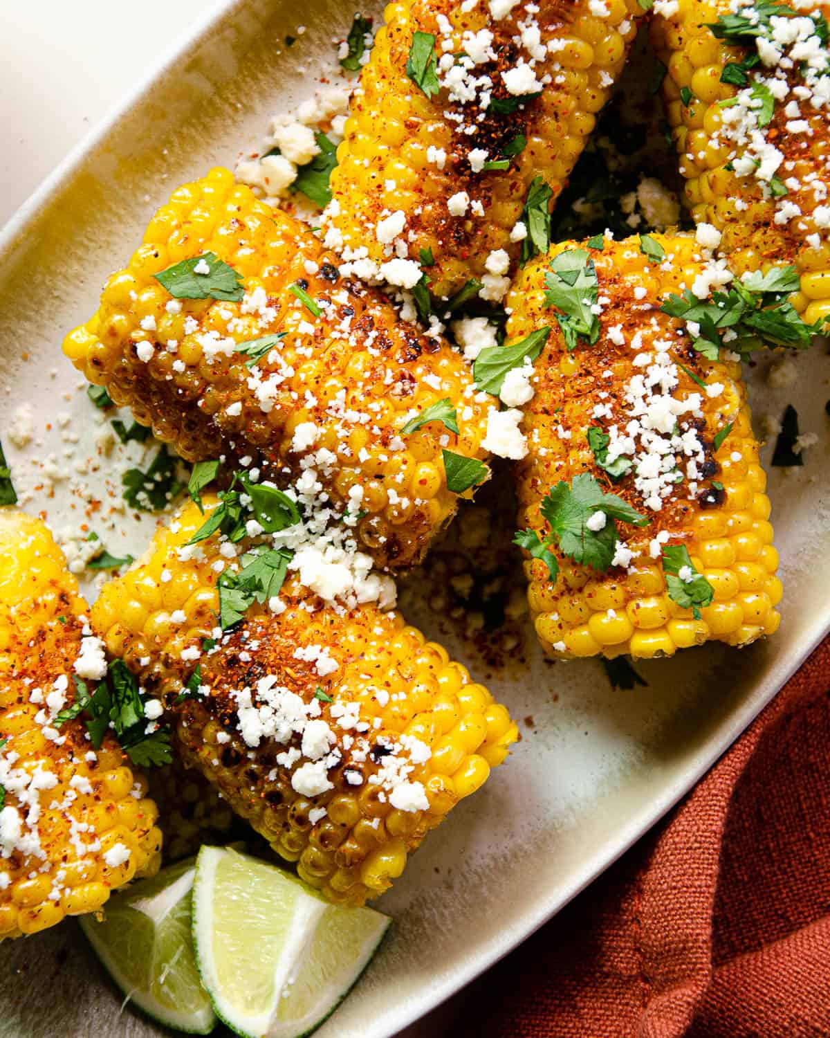 Close-up shot of Mexican street corn being held in hand, showing the beautiful contrast of white crema, red chili powder, and fresh green cilantro against golden charred corn kernels