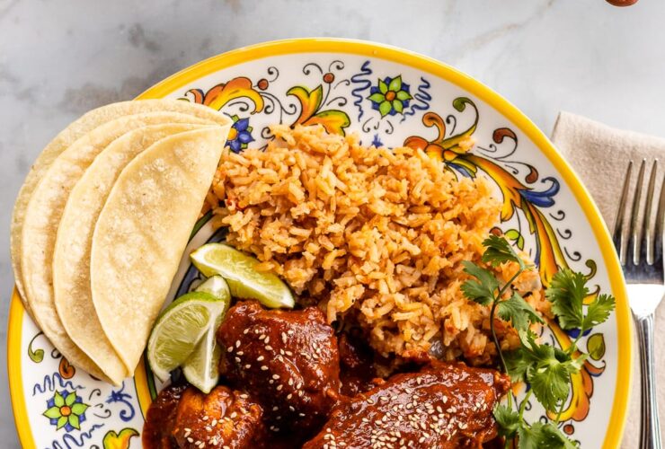 Mole poblano chicken served on white plate garnished with sesame seeds and cilantro with rice on the side