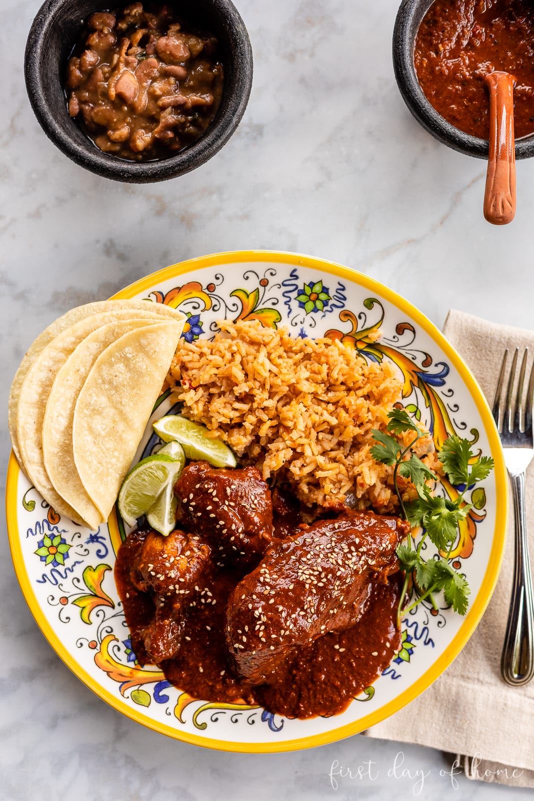 Mole poblano chicken served on white plate garnished with sesame seeds and cilantro with rice on the side