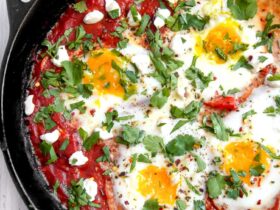 Vibrant shakshuka in cast iron skillet with perfectly poached eggs, fresh herbs, and warm crusty bread on rustic wooden table