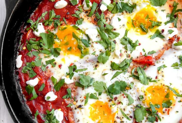 Vibrant shakshuka in cast iron skillet with perfectly poached eggs, fresh herbs, and warm crusty bread on rustic wooden table