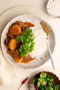 spicy shaved beef massaman curry in bowl with rice garnished with cilantro and lime
