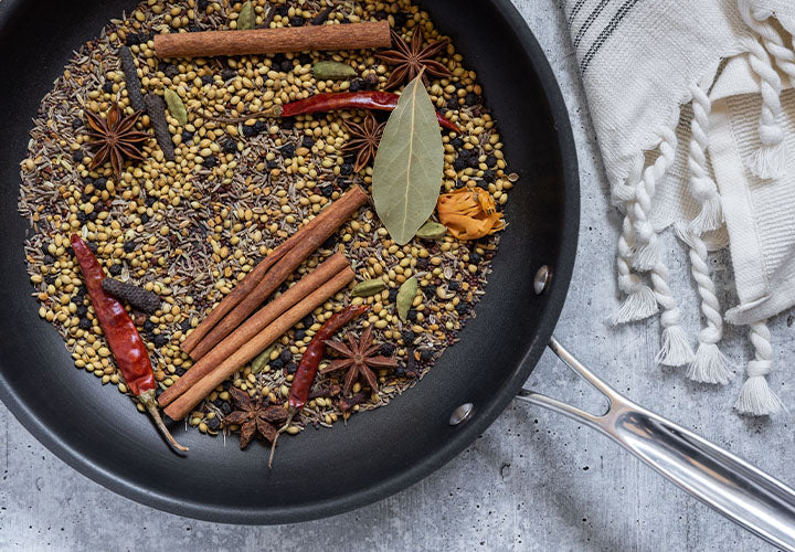 whole spices being toasted in a dry pan with charred onions and ginger on cutting board