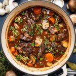 Elegant beef bourguignon in a rustic ceramic bowl with tender beef chunks, pearl onions, and mushrooms in rich wine sauce, garnished with fresh thyme