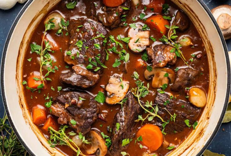 Elegant beef bourguignon in a rustic ceramic bowl with tender beef chunks, pearl onions, and mushrooms in rich wine sauce, garnished with fresh thyme
