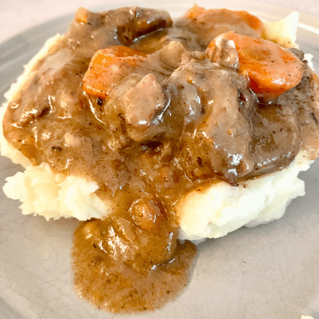Close-up shot of beef bourguignon served over creamy mashed potatoes with fresh herbs and a glass of red wine in the background