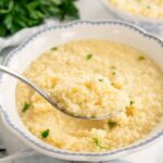 Creamy buttered pastina in a white ceramic bowl garnished with fresh parsley and grated Parmesan cheese