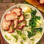 Beautifully glazed char siu pork sliced and arranged on a white platter with garnish of green onions and sesame seeds