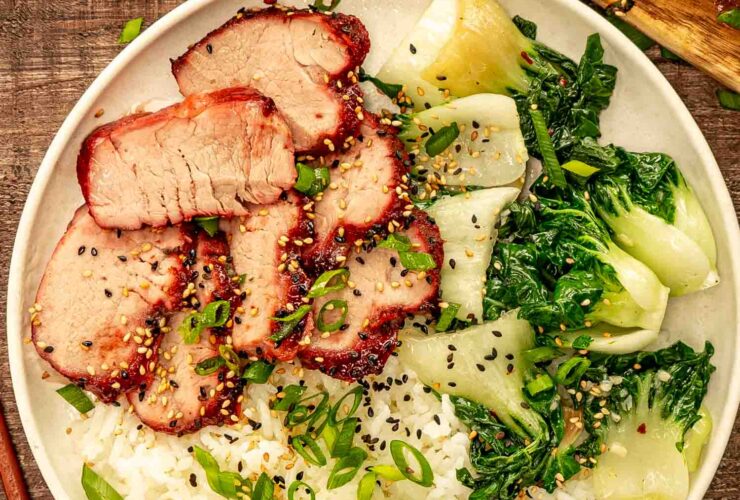 Beautifully glazed char siu pork sliced and arranged on a white platter with garnish of green onions and sesame seeds